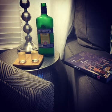 Photo of a plush interior with a book resting on the arm rest, and a pair of inviting adult beverages.